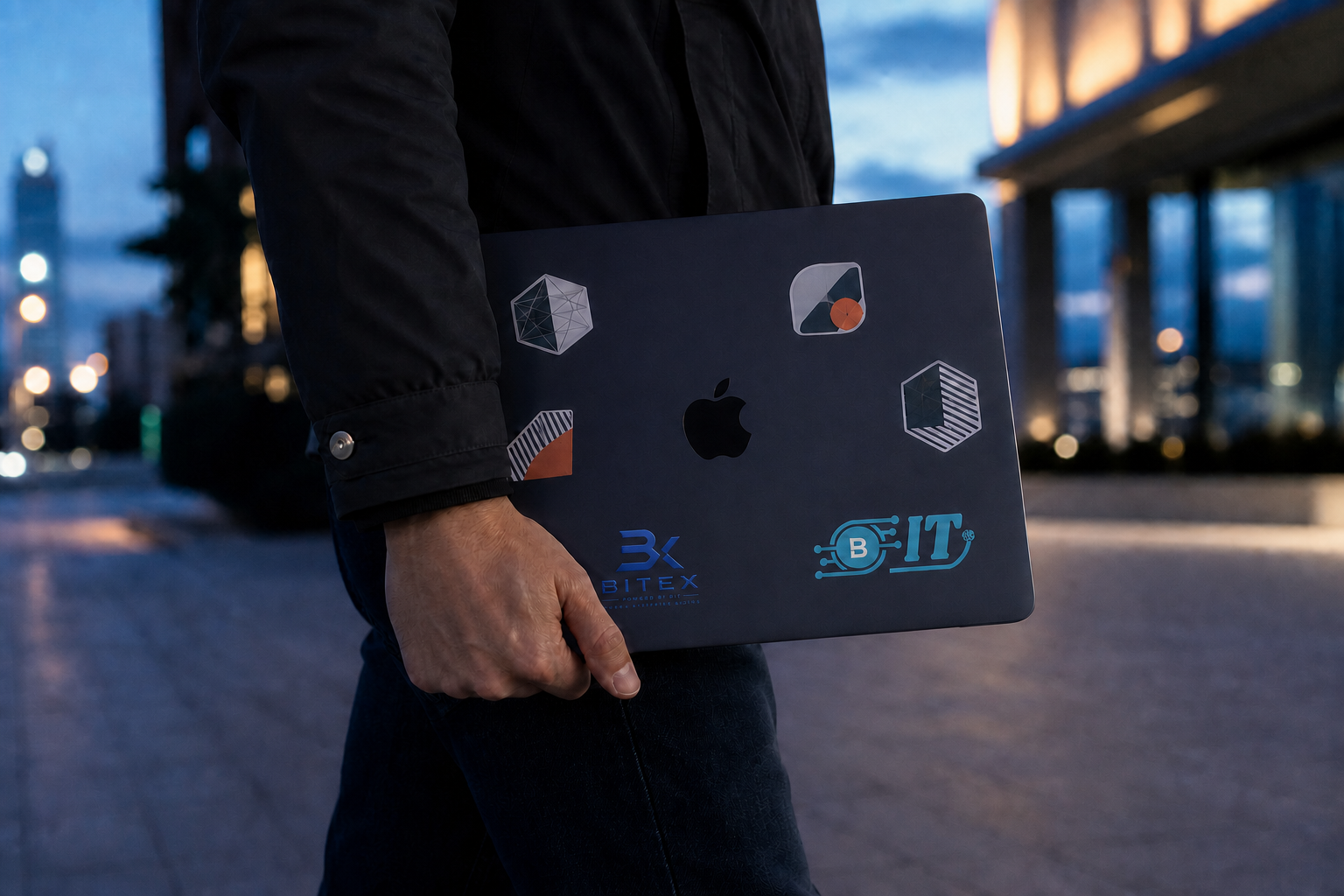 A Midnight MacBook with brand stickers being carried through a city